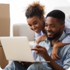 Couple look at laptop together, smiling.